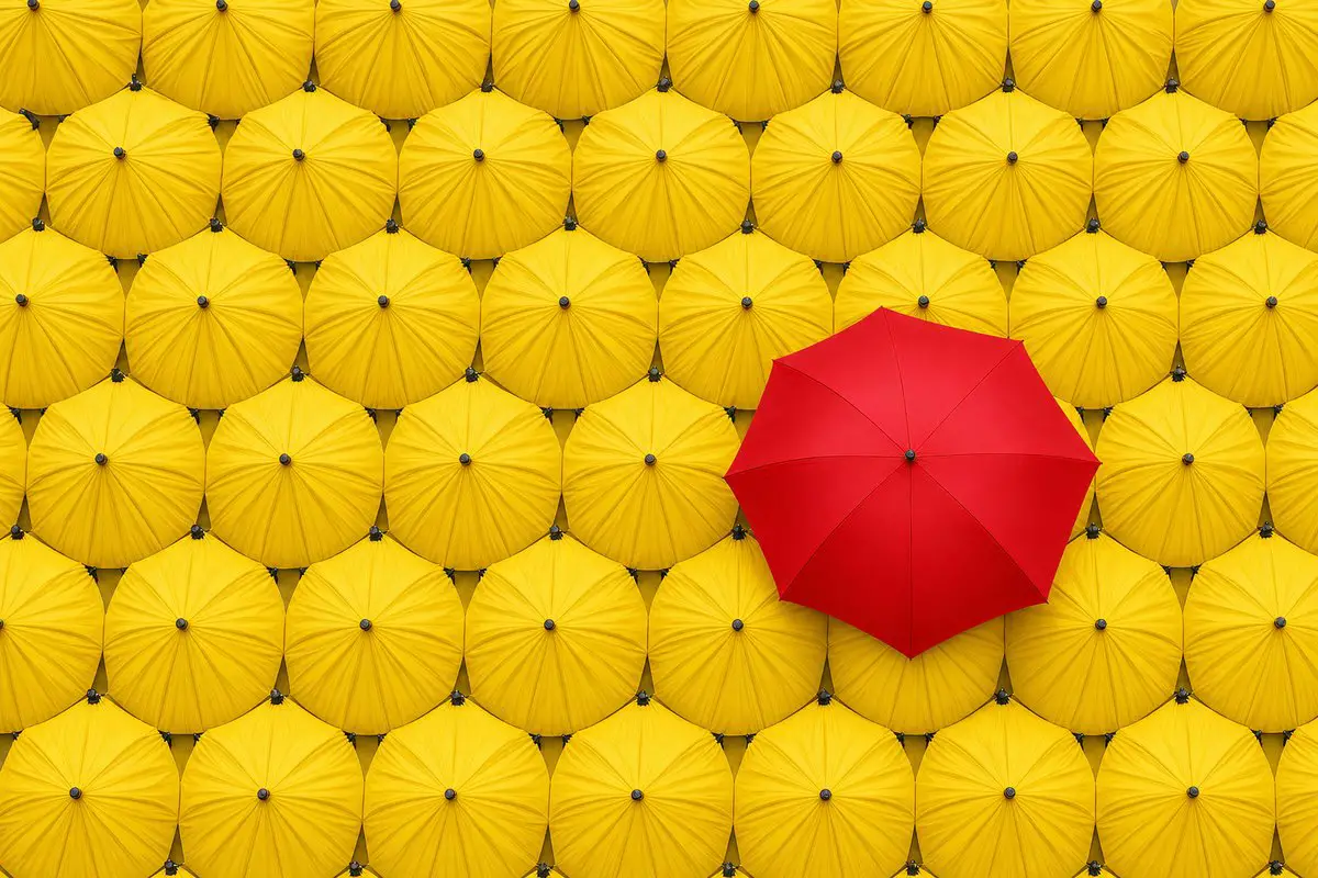 A repeating grid of identical yellow umbrellas with a single red umbrella breaking the pattern