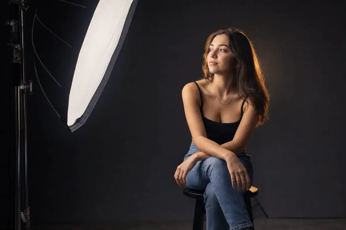 A portrait subject lit by a large softbox in a photography studio, showing soft directional lighting