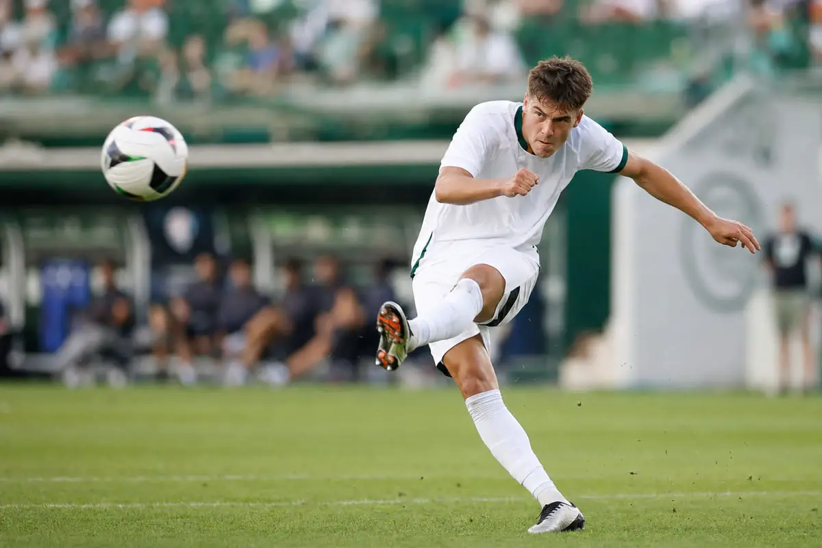 A soccer player captured tack-sharp mid-kick with the ball frozen in the air, blurred stadium background